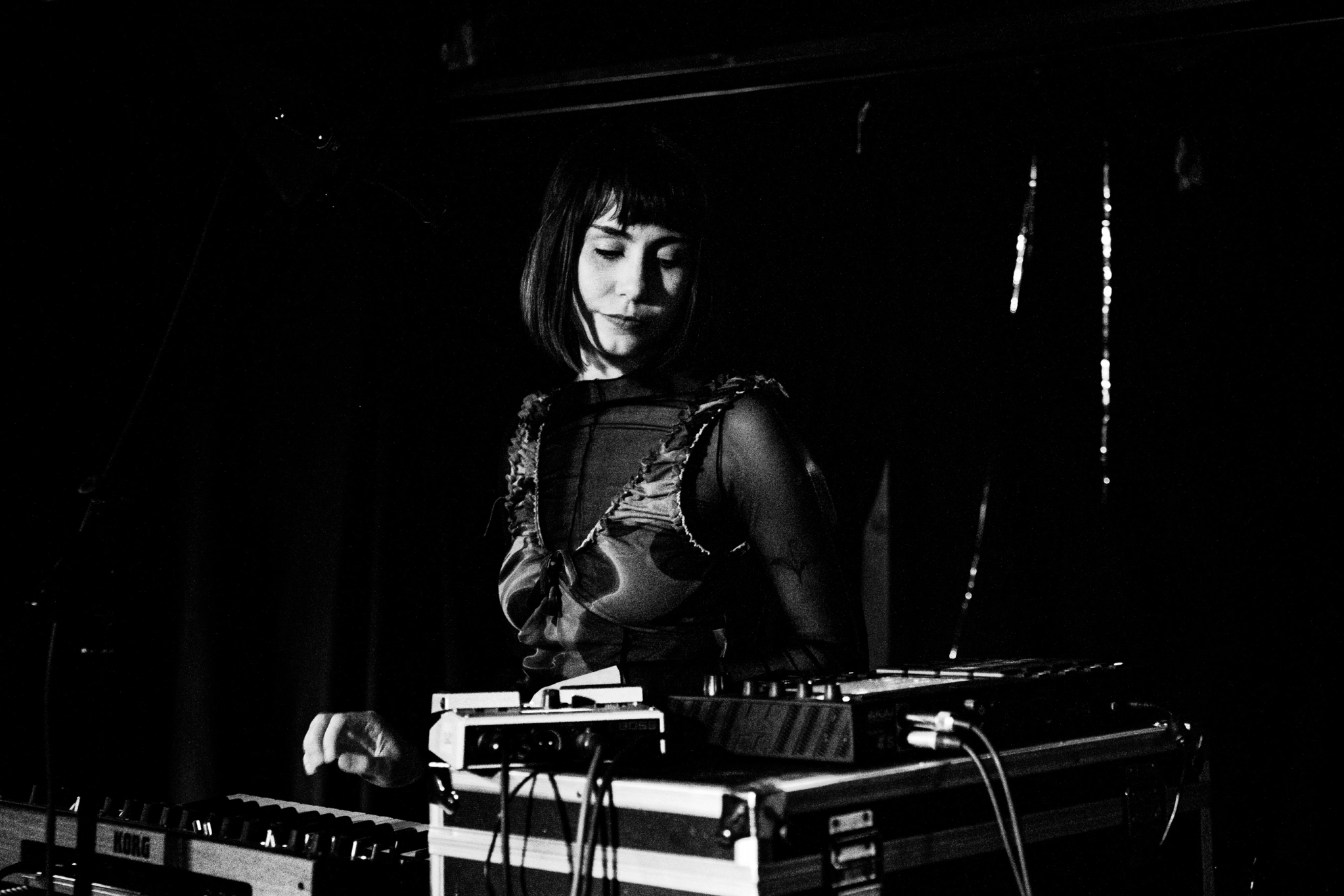 A black and white photo of Emily Zurowski on stage with synthesisers and a microphone
